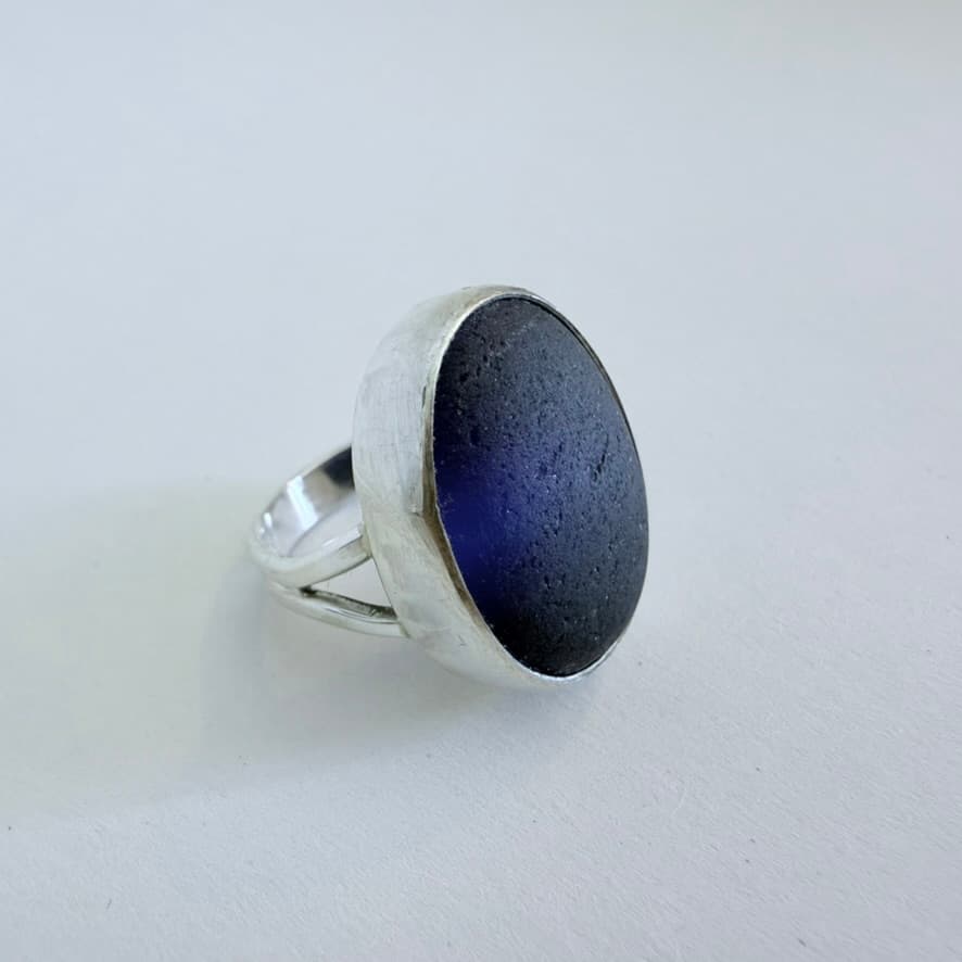 A handmade sterling silver ring set with a deep blue sea glass cabochon
